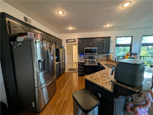 7730 N Shannon Ave, Kansas City, MO 64152 - kitchen with appliances with stainless steel finishes, a peninsula, a sink, decorative backsplash, and light stone counters