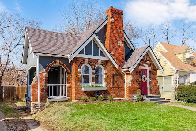 english style home featuring brick siding, a chimney, a front lawn, and fence