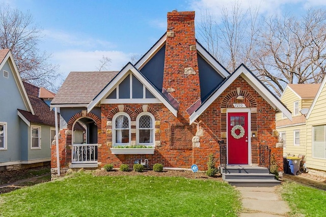 tudor house with a front lawn, brick siding, a chimney, and a shingled roof