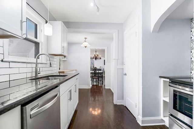 kitchen featuring dark stone countertops, dark wood-style floors, a sink, stainless steel appliances, and backsplash