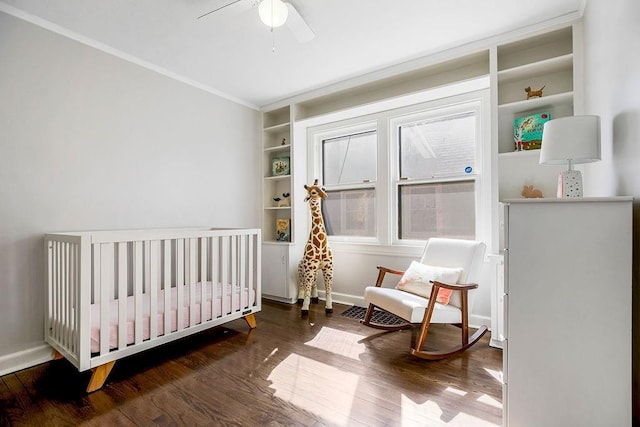 bedroom with wood finished floors, baseboards, ceiling fan, a crib, and ornamental molding