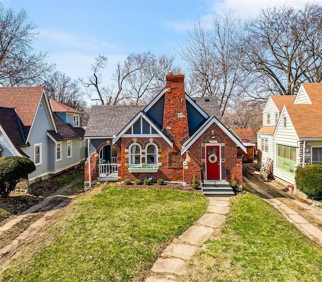 tudor home featuring brick siding, a chimney, and a front lawn