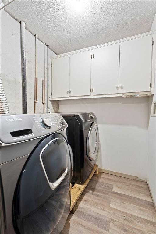 laundry area with cabinet space, separate washer and dryer, light wood-type flooring, and a textured ceiling