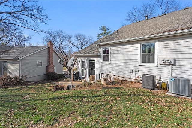 rear view of property with a yard, central AC, and a shingled roof