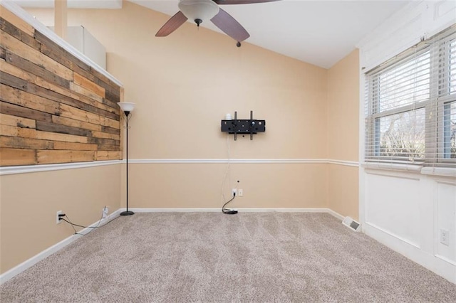 carpeted spare room with lofted ceiling, baseboards, visible vents, and ceiling fan