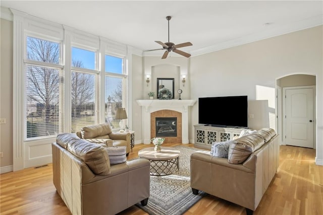 living room with light wood-type flooring, visible vents, ornamental molding, a tiled fireplace, and arched walkways