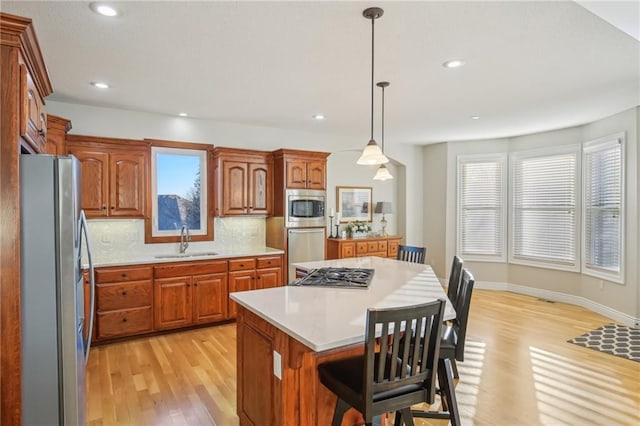 kitchen with light wood finished floors, a kitchen island, a sink, light countertops, and appliances with stainless steel finishes