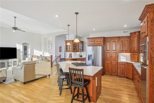 kitchen featuring brown cabinetry, a breakfast bar, arched walkways, light countertops, and appliances with stainless steel finishes