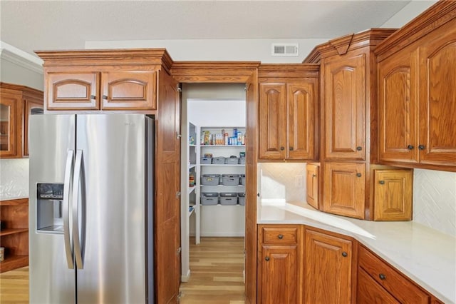 kitchen with visible vents, backsplash, brown cabinetry, stainless steel fridge with ice dispenser, and light countertops