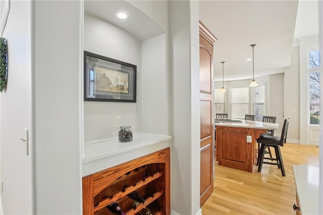 bar with baseboards, light wood-type flooring, recessed lighting, arched walkways, and hanging light fixtures