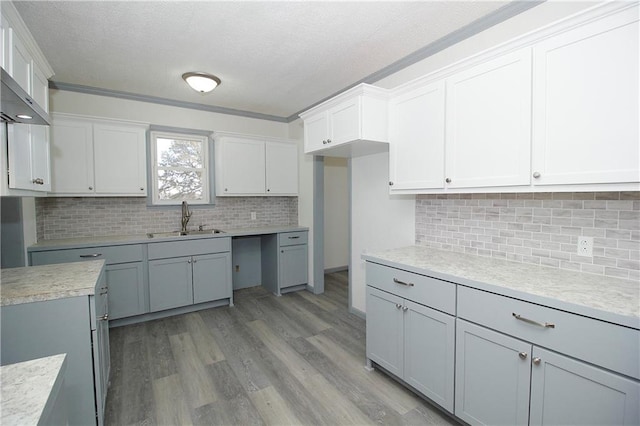 kitchen featuring light wood finished floors, a sink, a textured ceiling, white cabinetry, and light countertops