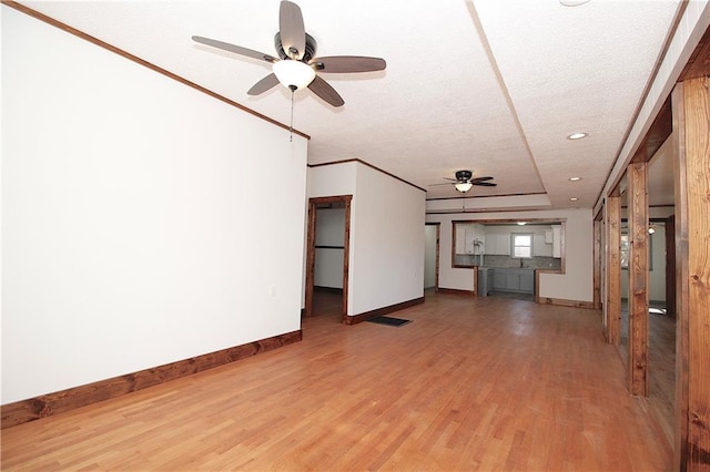 unfurnished living room with a ceiling fan, wood finished floors, baseboards, ornamental molding, and a textured ceiling