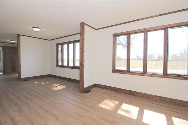 empty room with dark wood-style floors, visible vents, crown molding, and baseboards