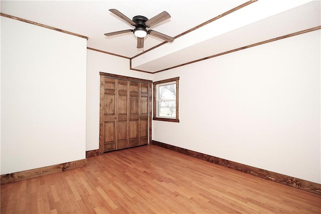 unfurnished bedroom featuring baseboards, ornamental molding, light wood-style floors, a closet, and a ceiling fan