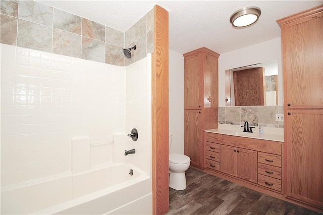 full bath with tub / shower combination, toilet, wood finished floors, a textured ceiling, and vanity