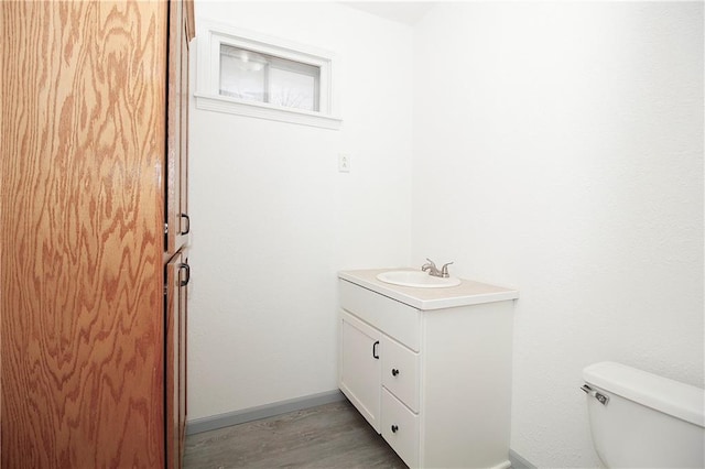 half bath with toilet, vanity, baseboards, and wood finished floors