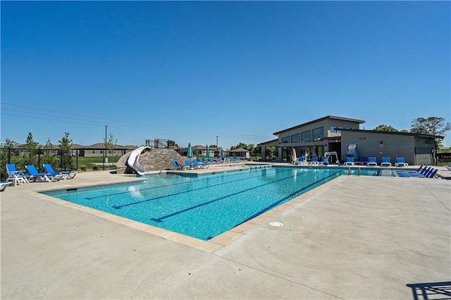 community pool with a water slide, a patio, and fence