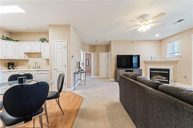 living room with a glass covered fireplace, visible vents, baseboards, and ceiling fan