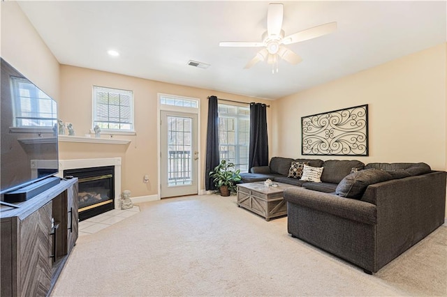 living area with visible vents, baseboards, ceiling fan, a fireplace with flush hearth, and light colored carpet