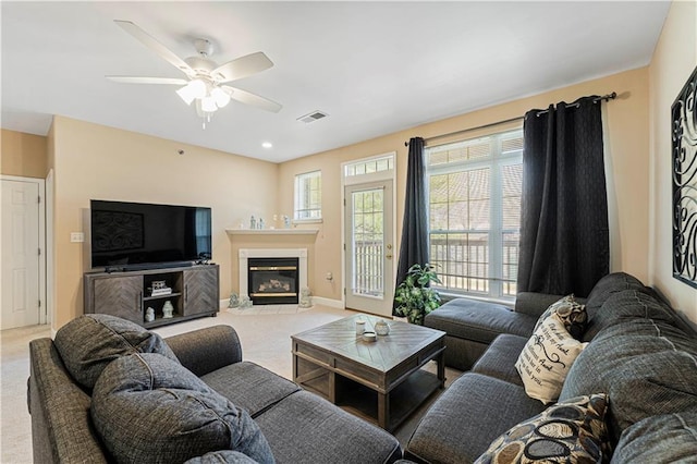 carpeted living area with a glass covered fireplace, a ceiling fan, visible vents, and baseboards