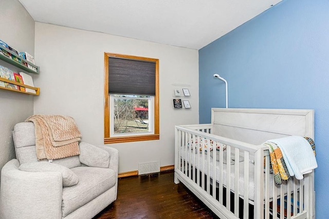 bedroom with visible vents, a crib, baseboards, and wood finished floors