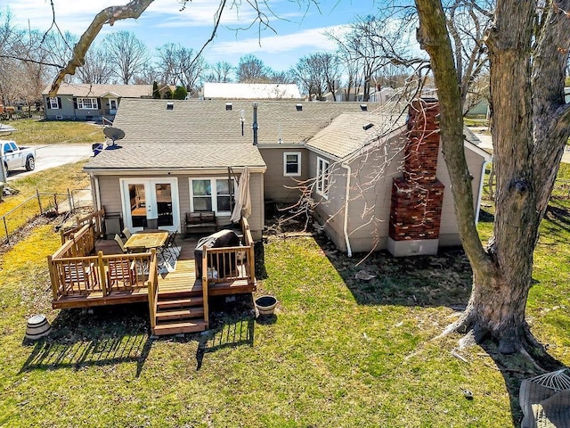 back of house featuring a lawn, a deck, fence, french doors, and roof with shingles