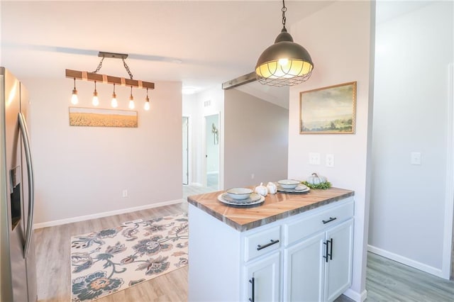 kitchen with decorative light fixtures, light wood-type flooring, vaulted ceiling, stainless steel fridge, and white cabinetry