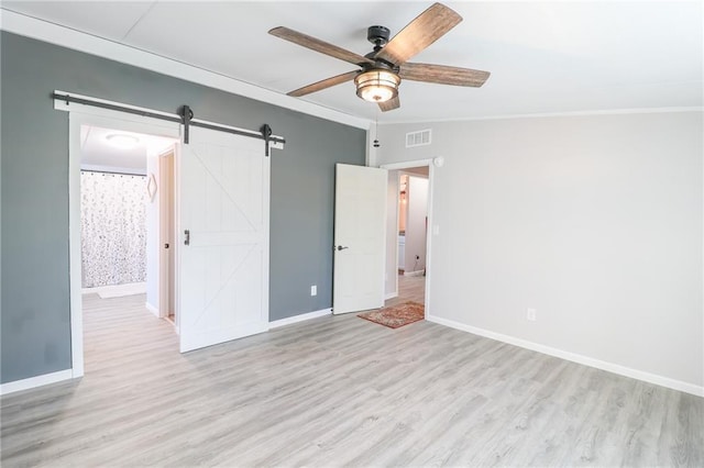 unfurnished bedroom with wood finished floors, visible vents, baseboards, crown molding, and a barn door