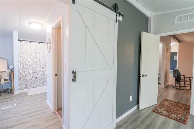 corridor featuring a barn door, baseboards, visible vents, and light wood finished floors