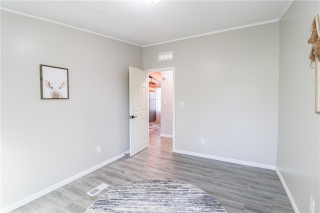 empty room with visible vents, baseboards, wood finished floors, and crown molding