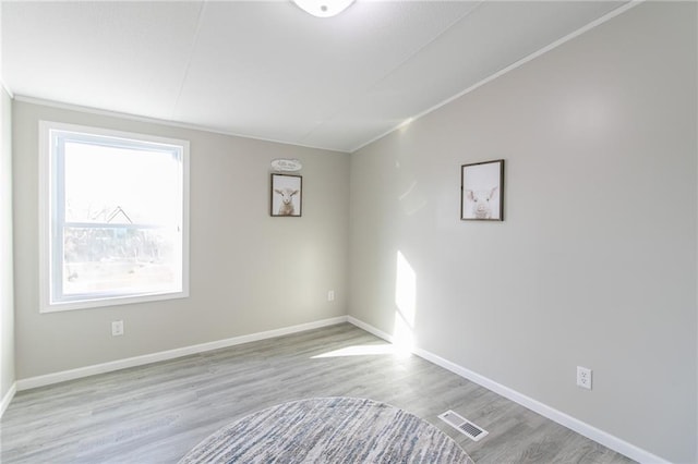 spare room with crown molding, wood finished floors, visible vents, and baseboards