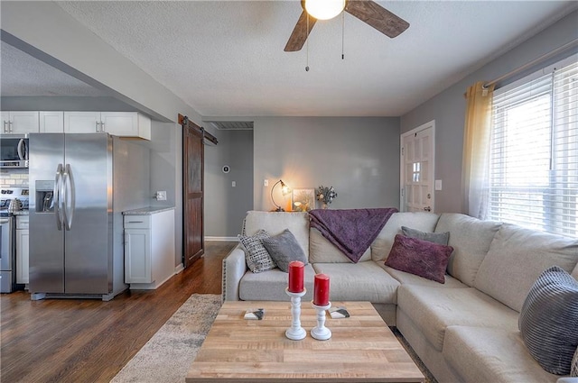 living area with a textured ceiling, a barn door, baseboards, ceiling fan, and dark wood-style flooring