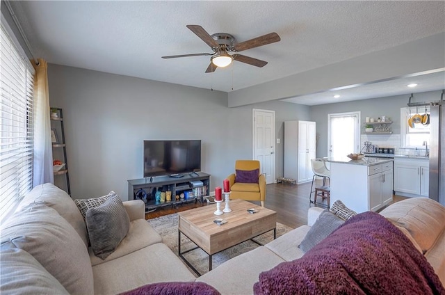 living area with dark wood-type flooring, a ceiling fan, and a textured ceiling