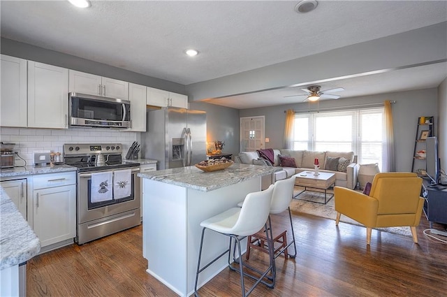 kitchen with a kitchen bar, dark wood-type flooring, white cabinetry, stainless steel appliances, and decorative backsplash