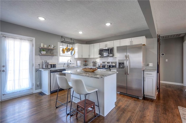 kitchen featuring a breakfast bar, a sink, white cabinetry, stainless steel appliances, and dark wood-style flooring