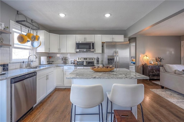 kitchen with dark wood-type flooring, a sink, tasteful backsplash, white cabinetry, and appliances with stainless steel finishes