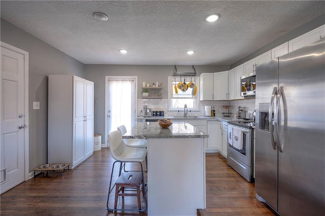 kitchen featuring a sink, a breakfast bar area, appliances with stainless steel finishes, and dark wood finished floors