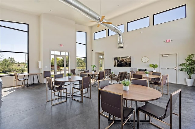 dining room featuring ceiling fan, baseboards, a towering ceiling, and finished concrete floors