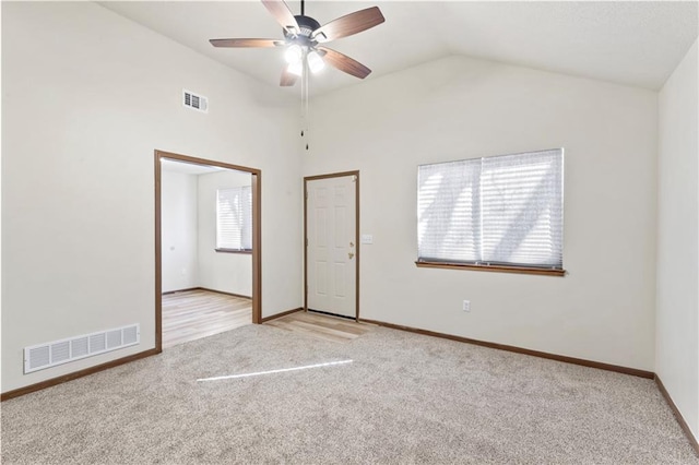 empty room featuring visible vents, light colored carpet, lofted ceiling, and ceiling fan