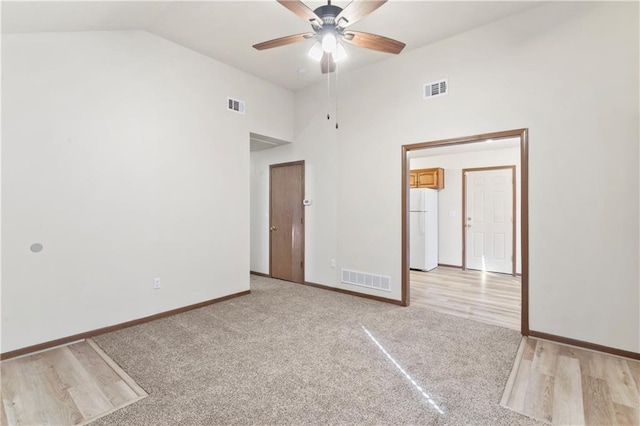 unfurnished bedroom featuring visible vents, baseboards, high vaulted ceiling, and freestanding refrigerator