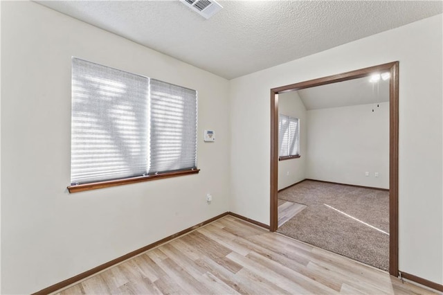 empty room featuring baseboards, light wood-style floors, visible vents, and a textured ceiling