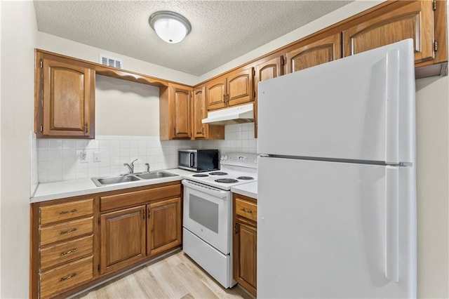 kitchen with visible vents, under cabinet range hood, a sink, white appliances, and brown cabinetry