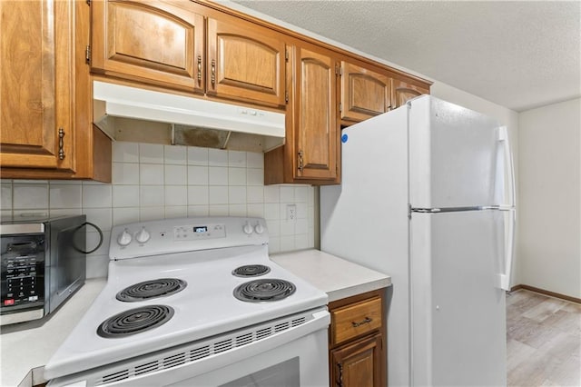 kitchen featuring tasteful backsplash, under cabinet range hood, light countertops, brown cabinetry, and white appliances