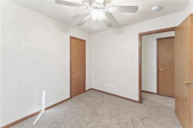 carpeted empty room with a textured ceiling, baseboards, visible vents, and ceiling fan