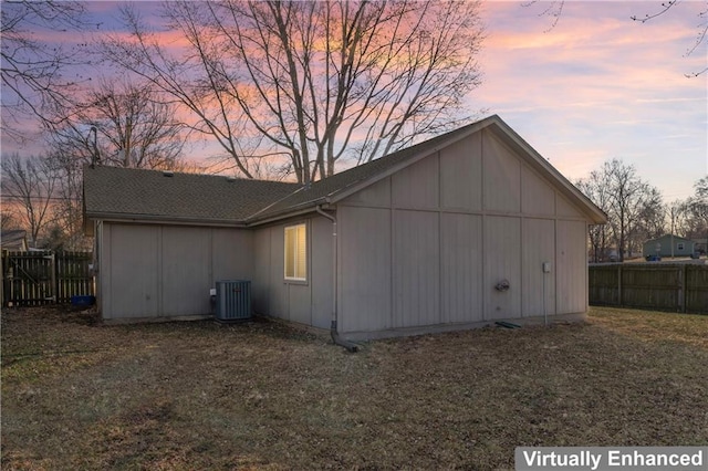 property exterior at dusk with board and batten siding, central AC, and fence