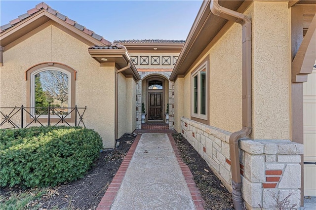 property entrance featuring stone siding, stucco siding, and a tile roof