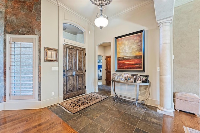 entrance foyer featuring crown molding, decorative columns, arched walkways, and baseboards