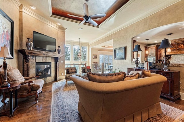 living area featuring a fireplace, a raised ceiling, dark wood-style floors, and ornamental molding