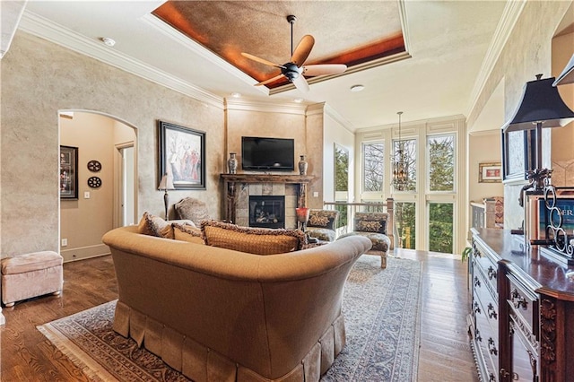 living room with a raised ceiling, wood finished floors, a fireplace, and arched walkways