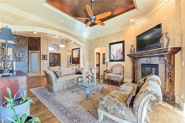 living room with arched walkways, crown molding, a tray ceiling, and wood finished floors